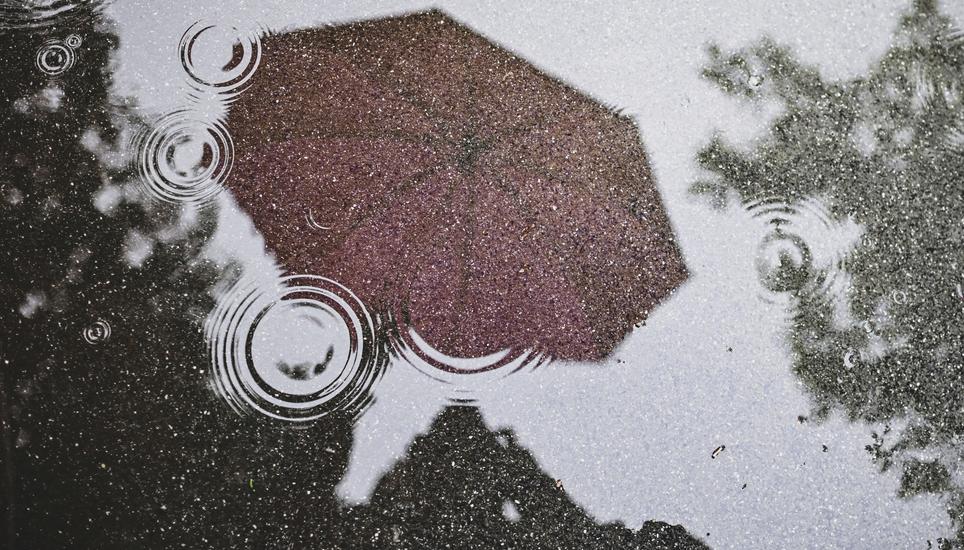 Ein knallig pinker Regenschirm spiegelt sich in einer Pfuetze auf dem grauen Asphalt. Wer an diesem regnerischen Tag vor die Tuer geht schuetzt sich mit einem Schirm. Wann kommt die Sonne wieder , am Dienstag, 21 Mai 2024. (Melanie Duchene / Schaffhauser 